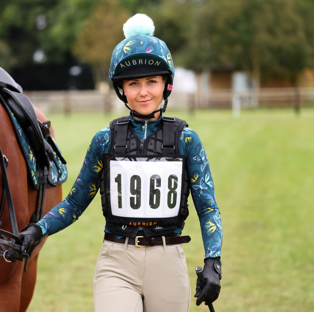 Woman in equestrian gear with a horse, wearing a helmet and an eventing cross country back number holder  with the number 1968.