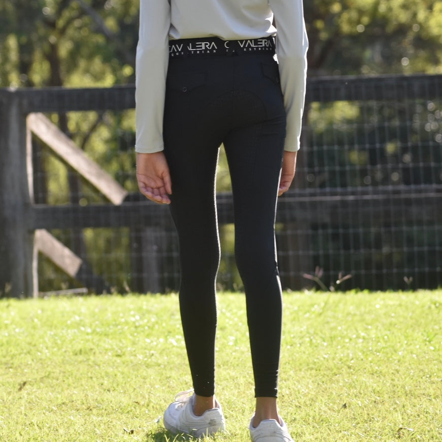 A girl wearing black everyday riding tights with a supportive elasticated waistband, standing on grass.